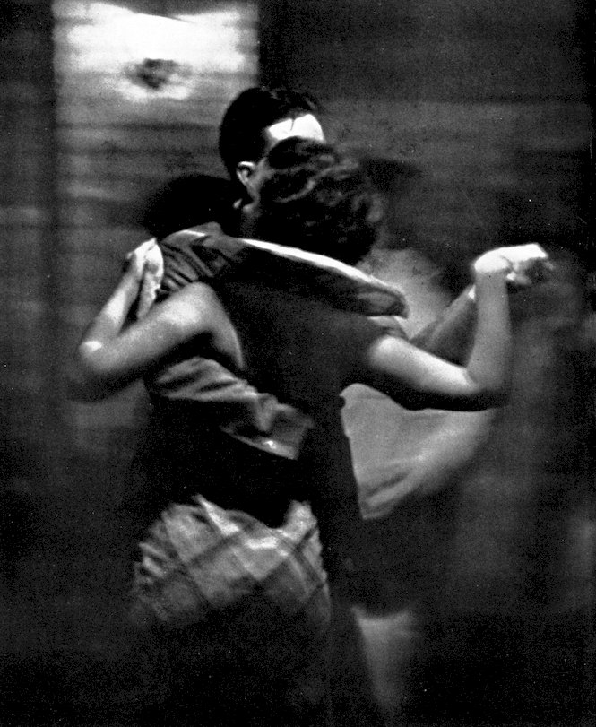 A moody, low-light black and white photograph of a couple dancing closely, captured with a slight motion blur.