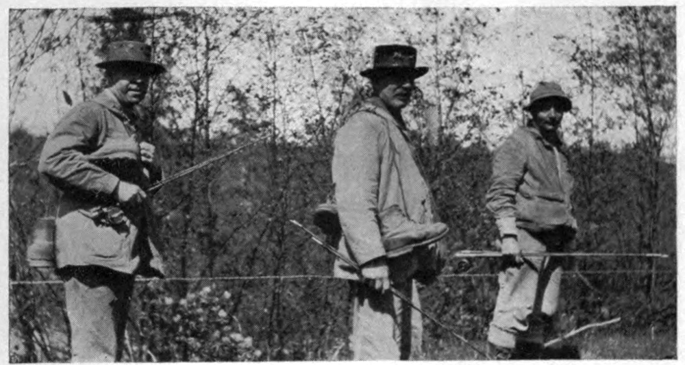 Photo of three men in the woods, wearing and carrying fishing gear.