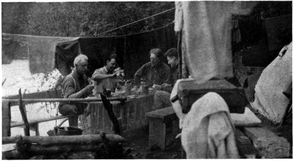 Photo of four men seated around a table under a dining fly.