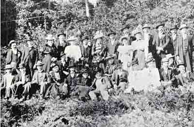 Rustic setting; many adults all in Sunday best, all wearing hats, men with walking canes.