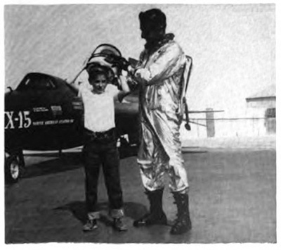 A boy trying on a helmet with aid froma man in a flight suit