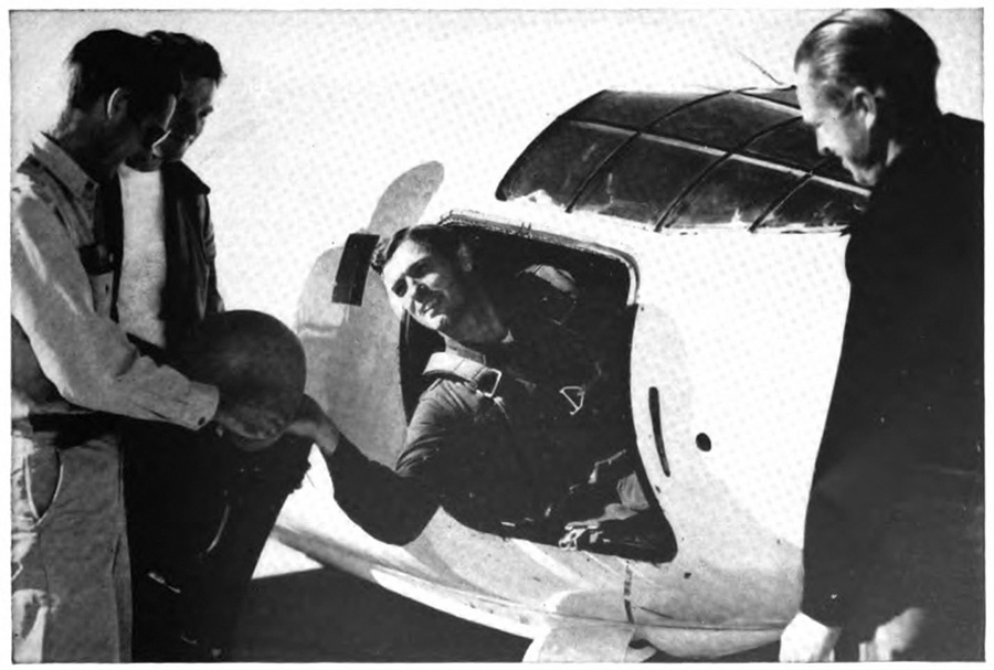 A man half out of a plane talking with three men standing next to it