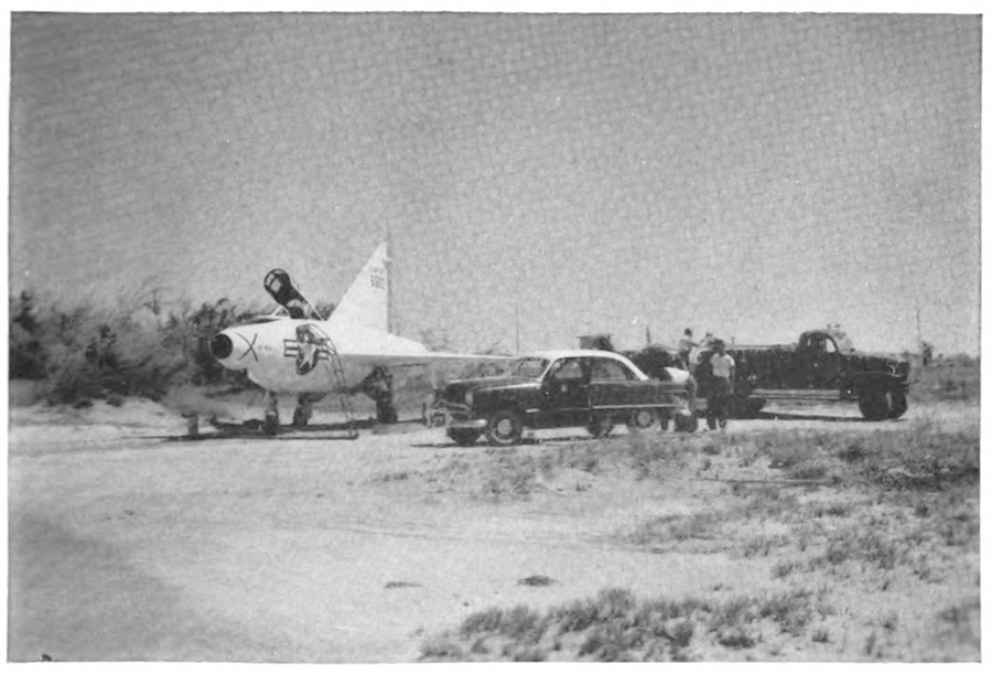 An airplane on a road with a car next to it, along with several people