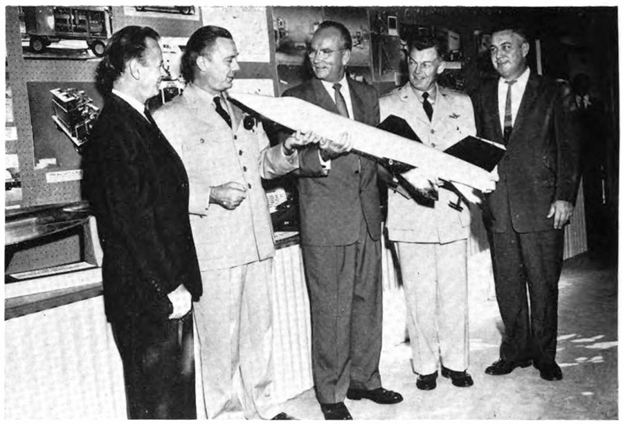 Five men standing, one holding a model aircraft
