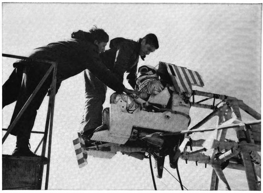 A pilot mounted in a simulation chair with two men assisting