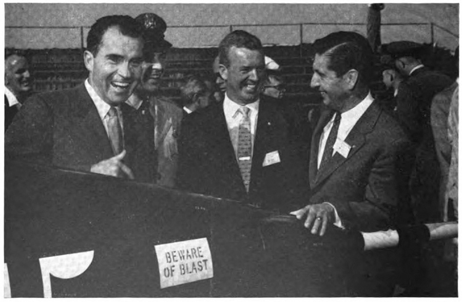 Picutre of three men laughing behind a sign saying 'beware of blast'