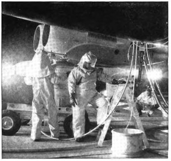 People in large protective suits around an airplane, with tubes hanging from it
